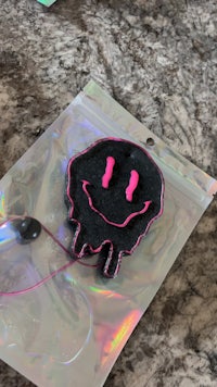 a black and pink air freshener with a smiley face on it